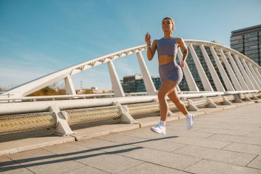 Modern binaların arka planında açık havada koşan aktif kadın sporcu.