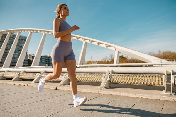 Active woman athlete is running an outdoor track on modern buildings background