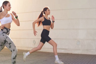 Günesli sabahlarda modern binalarda yan yana koşan iki aktif bayan atlet.