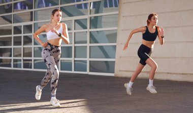 Spor giyim sektöründe iki genç kadın modern binalarda koşuyor. Etkin yaşam tarzı kavramı