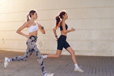 Spor giyim sektöründe iki genç kadın modern binalarda koşuyor. Etkin yaşam tarzı kavramı