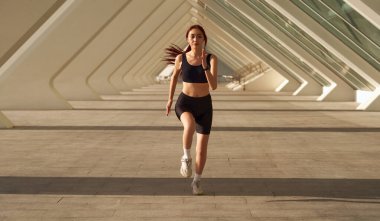 Güneşli bir günde dışarıda koşan spor kıyafetli genç bir bayan sporcu. Sabah koşusu