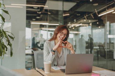 Neşeli ve pozitif bir iş kadını çağdaş ofis ortamında akıllı telefonuyla mutlu mesut meşgul oluyor.