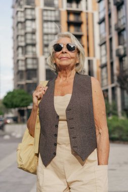 Kendinden emin yaşlı bir kadın canlı bir şehir zeminine ve çevreye karşı gururla modern moda sergiliyor.