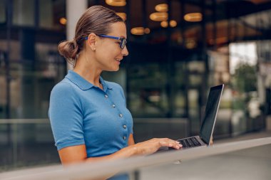 Modern çalışma kültürünü sergilemek için şık bir ofis ortamında dizüstü bilgisayar kullanan profesyonel bir kadın..