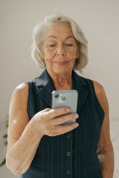 Изящная пожилая женщина, умело пользующаяся своим смартфоном, иллюстрирующая важную роль технологий в повседневной жизни