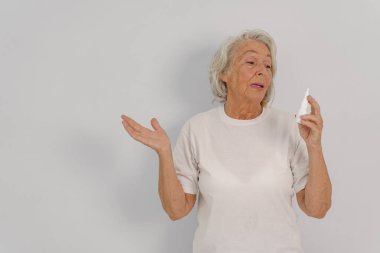 Yaşlı bir kadın zarif bir şekilde elinde bir cilt bakımı ürünüyle güzellik bakımına ve kendine olan güvenini gösteriyor.