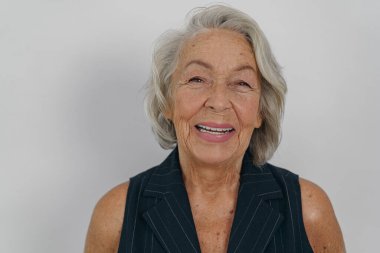 Yaşlı bir kadın enerjik bir şekilde poz verirken neşeli bir şekilde gülümser basit bir arka plana karşı.