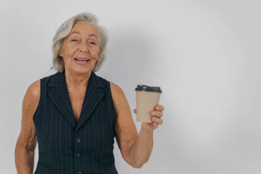 Neşeli yaşlı bir kadın neşeyle elinde dumanı tüten bir kahve fincanı tutuyor, sıcaklık, pozitiflik ve mutluluk saçıyor.