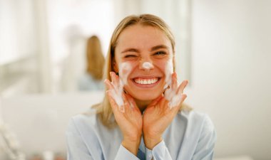 Mutlu bir kadın cilt bakımı yapıyor. Parlak bir banyoda güzelliğini sergiliyor.