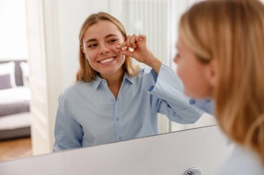 Parlak bir banyoda, genç bir kadın dişlerini fırçalıyor, diş hijyeninin ve kişisel bakımının önemini vurguluyor.