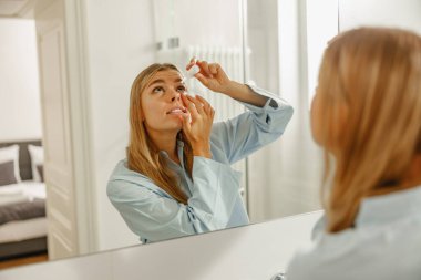 Şık ve modern bir banyoda, genç bir kadın güzel gözlerine göz damlası damlatarak özel ilgi gösterir.