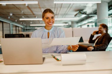 Neşeli bir iş kadını enerji dolu, parlak, çağdaş bir çalışma alanında önemli belgelerle meşgul olur.