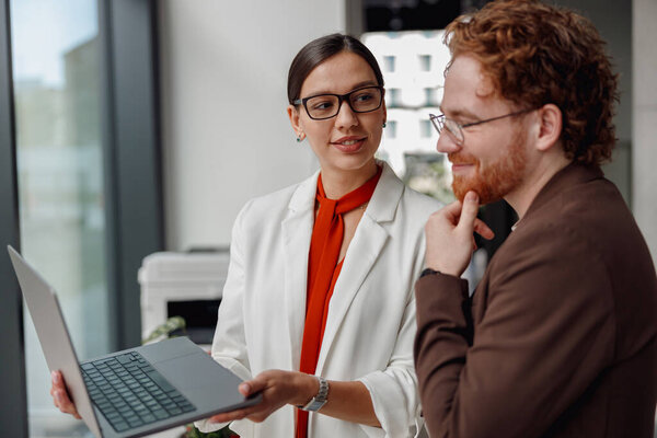 Двое коллег участвуют в динамичных дискуссиях об идеях во время совместной работы над ноутбуком в современном рабочем пространстве