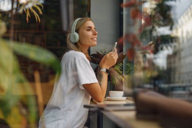 Tarz sahibi bir kadın kahvesini yudumlarken müzik dinlerken bir kafede dinlenir.