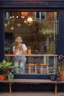 Rahat bir kafede yemyeşil bitkilerle kahve içen bir kadının sakin bir sahnesi.