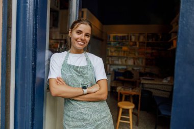 Neşeli ve neşeli bir barista, samimi kafesinin davetkar girişinde duruyor. Sıcak ve saf konukseverlik saçıyor.