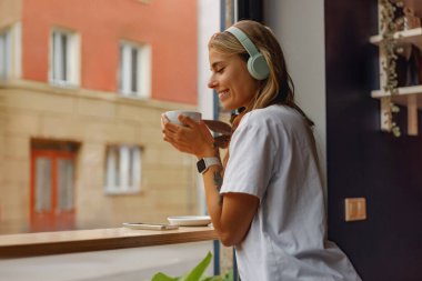 Bir kadın sıcak kahvesinin keyfini çıkarırken en sevdiği müziği dinleyip rahat bir ortam yaratıyor.