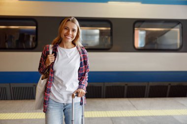 Elinde bavuluyla neşeli ve gülümseyen bir gezgin heyecanlı bir tren istasyonunda durur, maceraya hevesle hazırdır.