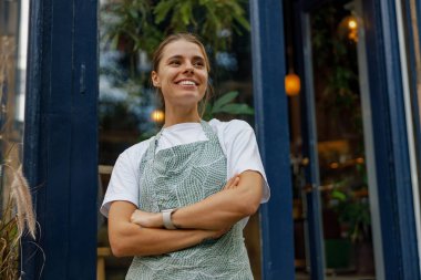 Neşeli ve arkadaş canlısı bir barista müşterileri karşılamaya hevesle hazır, hareketli bir kahve dükkanının önünde duruyor.