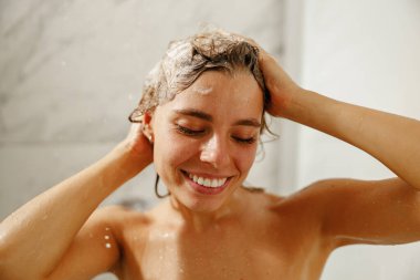 Bir kadın, modern ve şık bir banyoda saçlarını şampuanla yıkayarak ferahlatıcı bir duştan zevk alır.