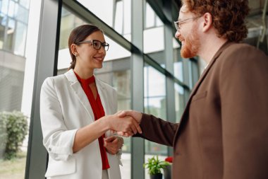 Modern bir ofiste, iki profesyonel, karşılıklı anlaşma ve işbirliğini sembolize ederek el sıkışıyor.