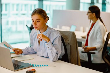 İki kadın, modern ve çağdaş bir ofis ortamında çalışma masalarında canlı bir atmosferi olan özenle çalışıyor.