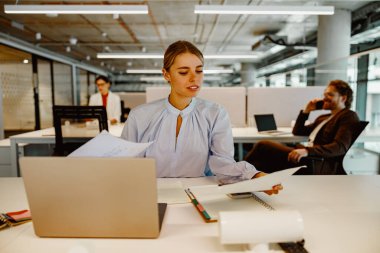 Modern bir ofis alanında çeşitli belgelerle çalışan özverili ve odaklanmış bir profesyonel.