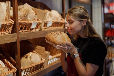 Genç bir kadın yoğun bir fırında taze ekmek kokusunun tadını çıkarıyor, çeşitli sanatsal ürünler sergiliyor.