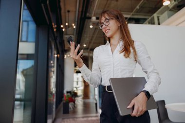 Moda ve tarz sahibi bir iş kadını, çağdaş bir ofis ortamında telefonuyla aktif olarak meşgul oluyor.