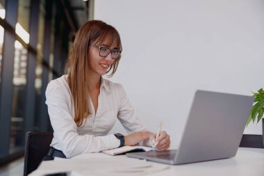 Kendini işine adamış ve işine odaklanmış bir iş kadını özenle dizüstü bilgisayarında şık, modern bir ofis çalışma alanında daktilo yazıyor.