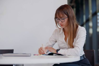 Kendini işine adamış ve profesyonel bir kadın modern bir çalışma ortamında çalışırken fikirlerini düzenli olarak not alır.