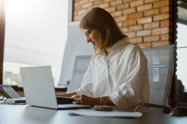 Şık bir ofis ortamında dizüstü bilgisayarda yazan odaklanmış bir kadın üretkenlik ve yaratıcılığı yakalıyor..