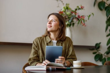 Genç bir kadın, şık bir kafe ortamında tabletini kullanırken derin bir yansıma anında neşe bulur.