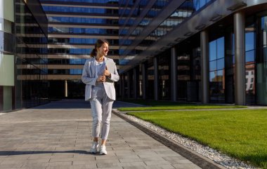 Zarif bir takım elbise giymiş profesyonel bir kadın modern ofis ortamında rahatça yürüyor.