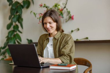 Genç bir kadın, yemyeşil bitkilerle dolu çağdaş bir çalışma alanında laptopuna derinden odaklanmıştır.