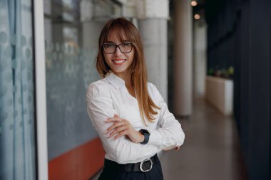 Profesyonel bir kadın, modern ve çağdaş bir ofis ortamında özgüven ve duruş içinde durur.