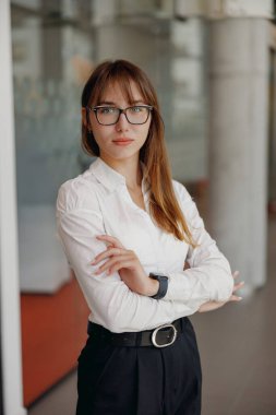 Şık gözlüklü, kendine güvenen profesyonel bir kadın modern ofis ortamında dengede duruyor.