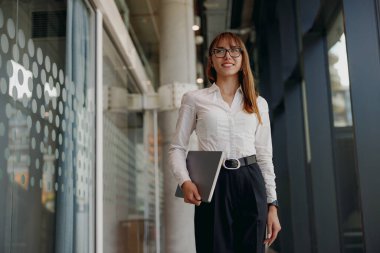 Profesyonel bir kadın, şık ve modern bir ofis ortamında kendine güvenerek gülümsüyor.