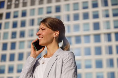 Kendine güvenen bir kadın dışarıda telefonla konuşuyor ve modern iş yaşamındaki rolünü sergiliyor.