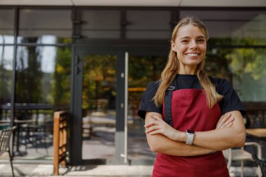 Modern bir kafenin dışında müşterilere hizmet etmeye hazır neşeli bir barista.