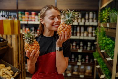 Canlı bir market ortamında, neşeli bir kadın mutlu bir şekilde taze ananasları kucaklıyor, mutluluk ve neşe saçıyor.