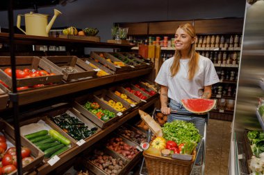 Neşeli bir kadın canlı bir organik pazarda taze ve renkli sebze ve meyveler seçiyor.