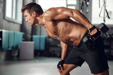 Formda bir adam modern bir spor salonunda dambılla egzersiz yapar. Güç ve kendini adamışlık gösterir..