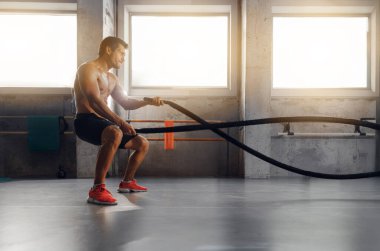 Odaklanmış bir adam güneşli bir spor salonunda halat egzersizleri yapıyor. Güç ve kararlılık gösteriyor..