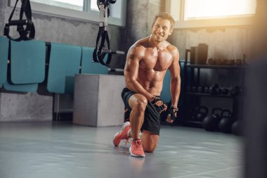 Kaslı bir adam şık bir spor salonunda spor yapar. Gücünü ve vücut geliştirmeye olan bağlılığını gösterir.