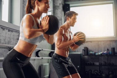 Formda bir çift, spor salonunda güç ve takım çalışması sergilemek için ilaç toplarıyla güçlü bir antrenman yapar.