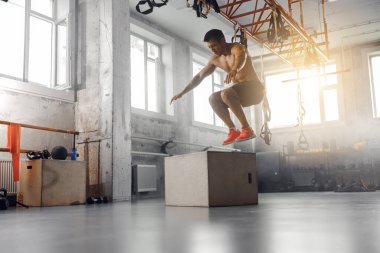 Atletik bir birey dinamik bir atlama egzersizi sergiliyor. İyi aydınlatılmış ve geniş bir spor salonunda.