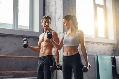 Kendine güvenen bir çift modern, kuytu bir spor salonu ortamında zorlu bir kaldırma seansına katılıyor.