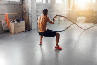İnanılmaz fit bir birey, parlak ve endüstriyel bir spor salonu içinde yoğun bir ip egzersizi yapıyor.